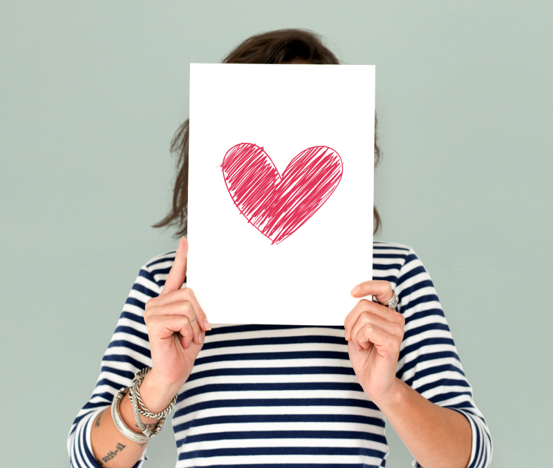 Woman holding red heart drawing on white paper